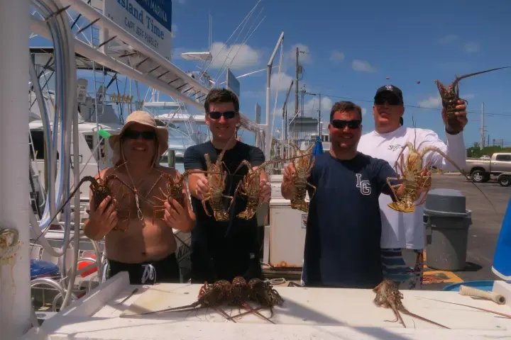 Four people at an Islamorada marina dock holding up spiny lobsters caught during a Florida Keys lobster diving charter