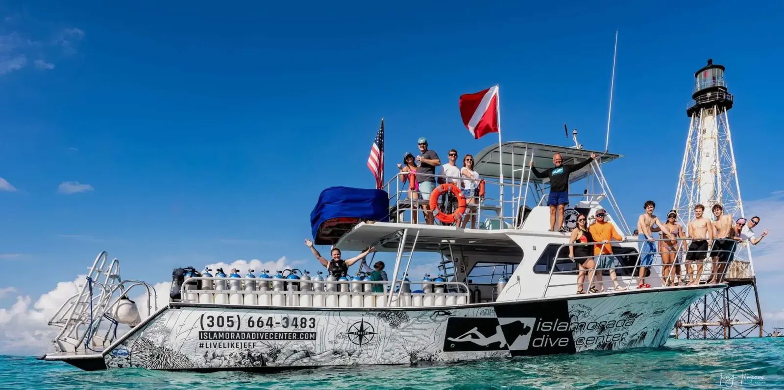 Group of people on Florida Keys Dive Center dive boat in clear blue water near Alligator lighthouse under a bright blue sky.