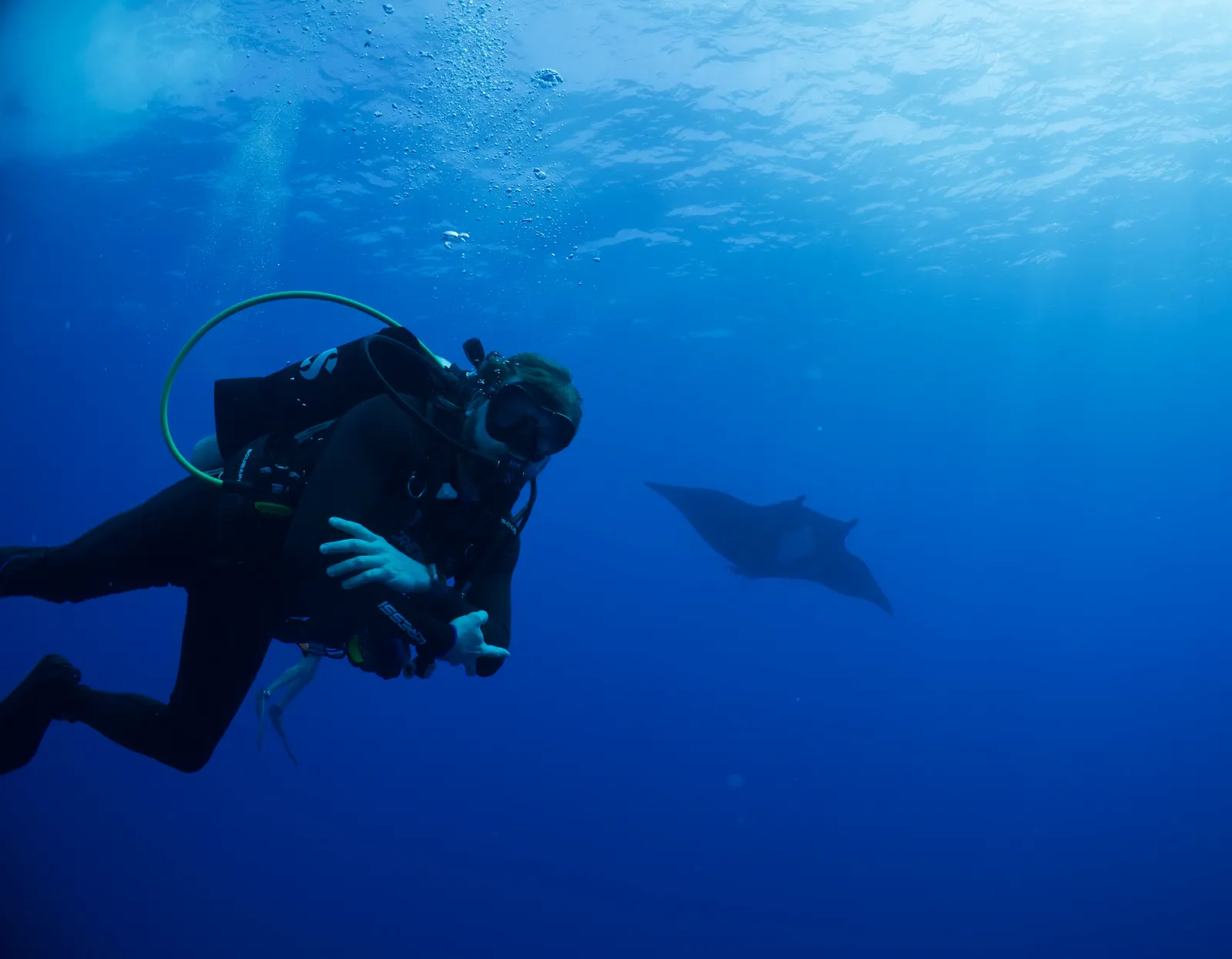 Scuba diver underwater near a manta ray in deep blue ocean.