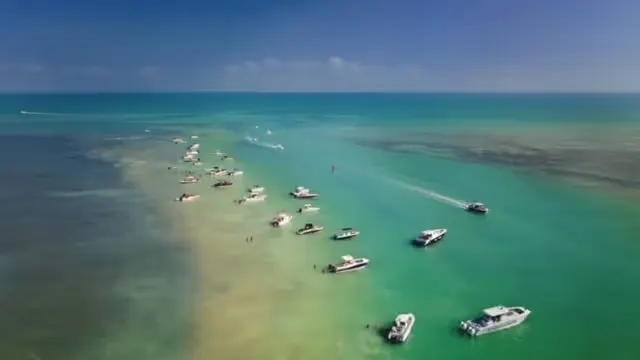 Boats anchored along a sandbar in clear turquoise ocean under a blue sky.